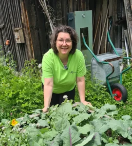 Nadja lehnt sich ans Holzhochbeet und lächelt in die Kamera